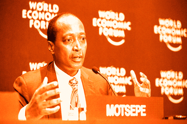 Patrice Motsepe speaking at a World Economic Forum panel, wearing a grey suit and striped tie, with his nameplate in front of the microphone.