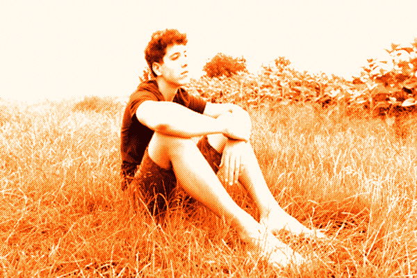Young man sitting barefoot in a field of tall grass, looking thoughtfully into the distance, rendered in the signature orange monochrome filter of BillionaireGambler.co.uk.